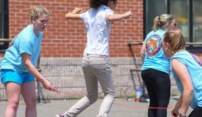 A group of students in blue shirts play jump rope with a child in a white shirt.