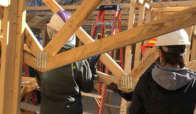 People in hard hats build with wood on a construction site.