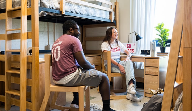 Two students sit in chairs in a dorm room.