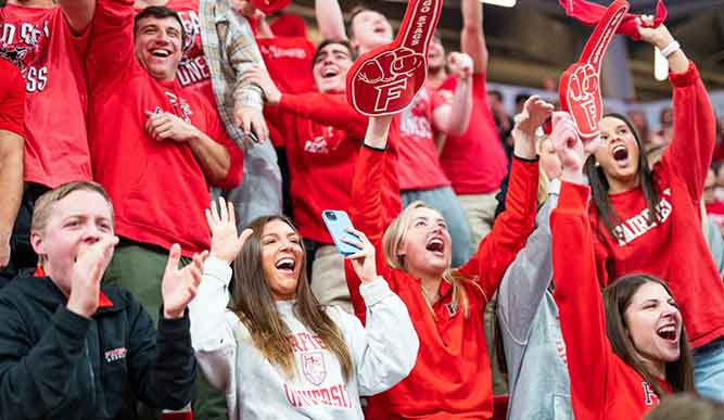 A diverse group of people in red shirts enthusiastically cheering together, showcasing excitement and unity.