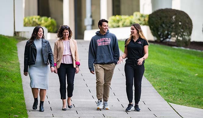 A group of students walk outdoors on a stone brick path.