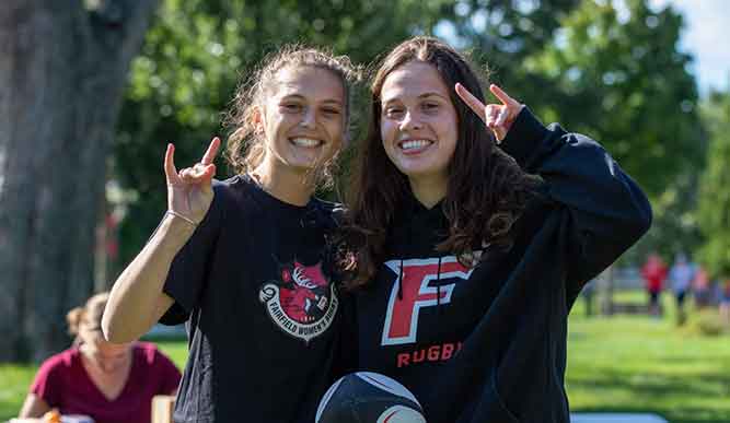 Two students holding a soccerball hold up their hands in a stag shape.