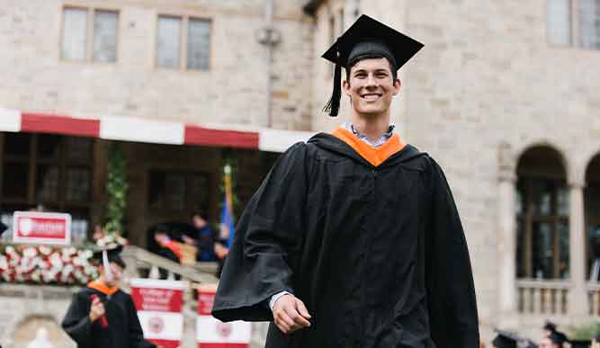 Student walking down Bellarmine Lawn smiling after receiving their diploma at Commecnement.