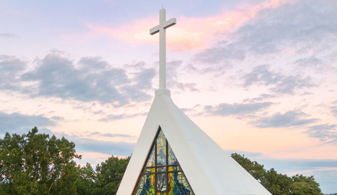 A photo of the top of the Egan Chapel with the white cross lit up by the sun.