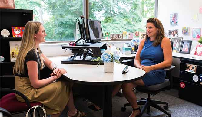 A staff member and student have a discussion in an office.