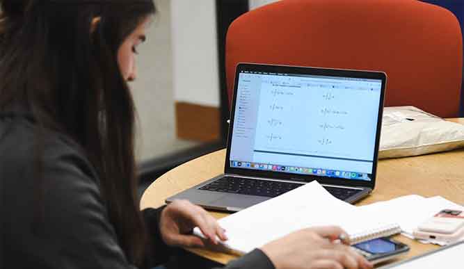 A student reads through their notes in front of an open laptop screen.