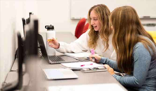 Two people sit in front of an open laptop with notebooks.