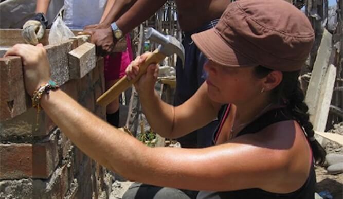 A student holds a hammer in front of a wooden fence.